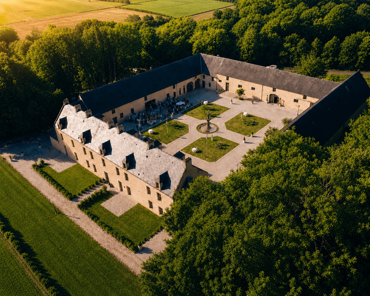 Vue aérienne du Domaine de la Cour des Lys à l'heure dorée — ancien relais postal du XVIIᵉ siècle, Cour d'Honneur de 1500 m² avec sa fontaine d'époque en son centre, cocktail dressé pour une réception